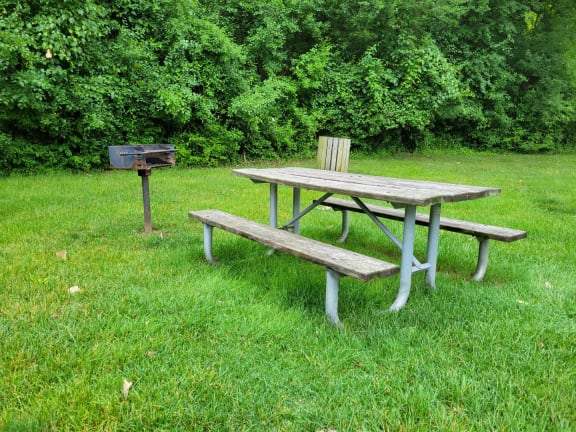 a picnic table and bench in a grassy area next to a grill at Cordoba Apartments, Farmington Hills, MI