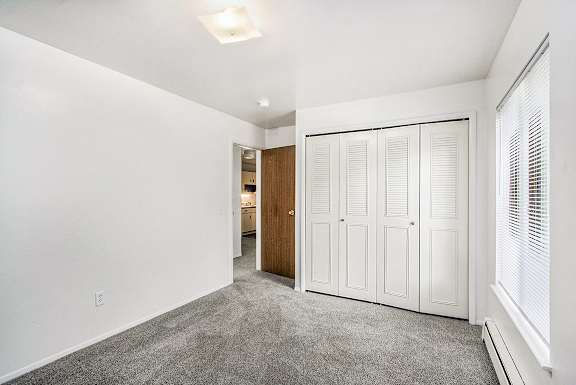 A bedroom with a large window, closet and grey carpet at Concord Place Apartments, Kalamazoo, MI