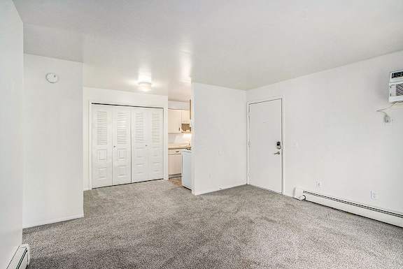 A large empty living/dining room with a carpeted floor and a large closet at Concord Place Apartments, Kalamazoo, MI