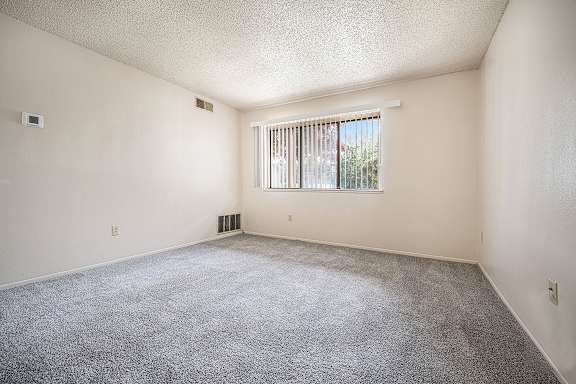 A living room with a carpeted floor and a window with blinds at Concord Place Apartments, Kalamazoo, MI, 49009