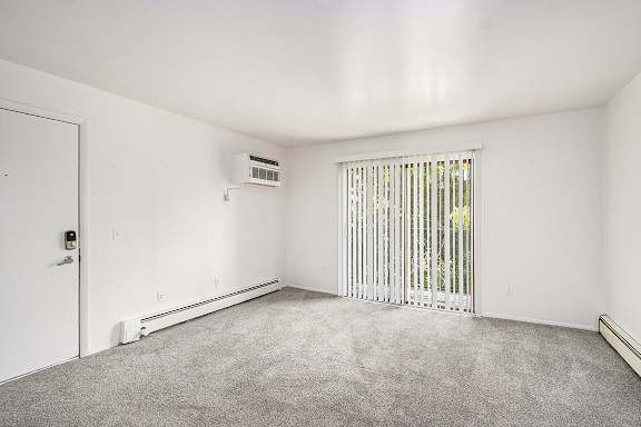 A living room with a slider to a balcony, blinds, and a carpeted floor at Concord Place Apartments, Kalamazoo, MI