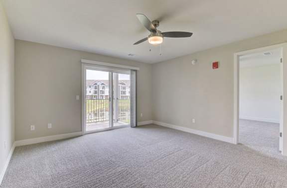 A living room with a ceiling fan and carpeted floor leading to a private balcony at Copper Creek Apartment Homes, Maize, Kansas