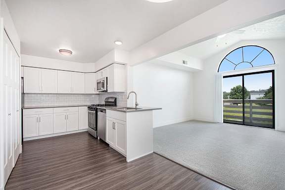 A kitchen with white cabinets and a living room with cathedral ceiling at The Crossings Apartments, Grand Rapids