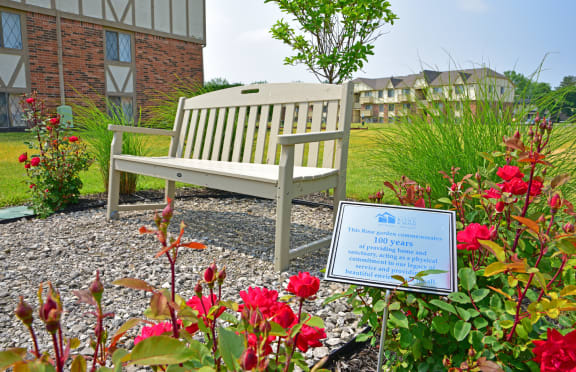 a bench in a garden with flowers and a sign at Huntington Place Apartments, Michigan, 48732