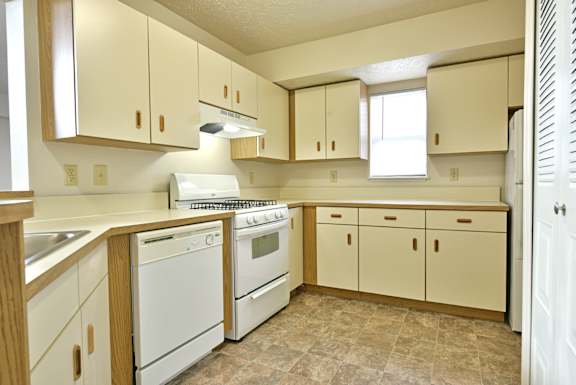 Galley kitchen with white appliances and wood trim cabinets at Heatherwood Apartments, Grand Blanc, 48439