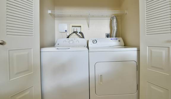 Fullsize washer and dryer with overhead wire shelf at Heatherwood Apartments, Grand Blanc, Michigan