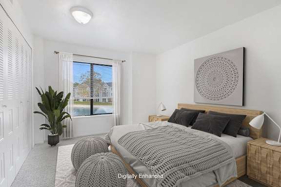 A bedroom with a large bed and a large window with a view at Dupont Lakes Apartments in Fort Wayne, IN