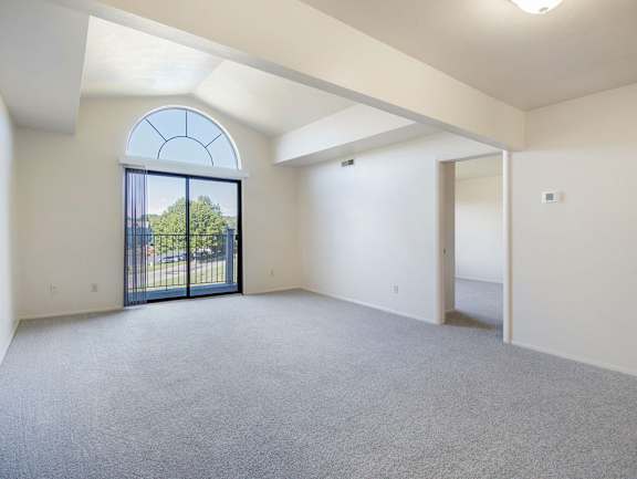 A spacious living room with a cathedral ceiling, large arched window and a carpeted floor at Dupont Lakes Apartments in Fort Wayne, IN