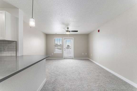 A spacious living room with a ceiling fan and a door leading to a private patio at Eagle Ridge Apartment Homes, Traverse City, Michigan