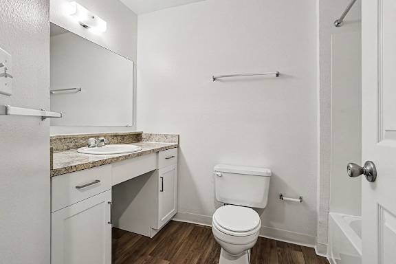 A white bathroom with a toilet, sink, and mirror at Emerald Park Apartments, Kalamazoo, Michigan
