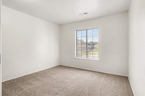 A bedroom with a carpeted floor and a window with a view at Emerald Park Apartments, Kalamazoo, Michigan