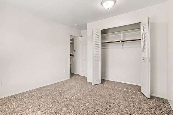 A white closet with a carpeted floor and a white door at Emerald Park Apartments, Kalamazoo, Michigan