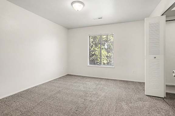 A bedroom with a window and a door to a walk-in closet at Emerald Park Apartments, Kalamazoo, Michigan