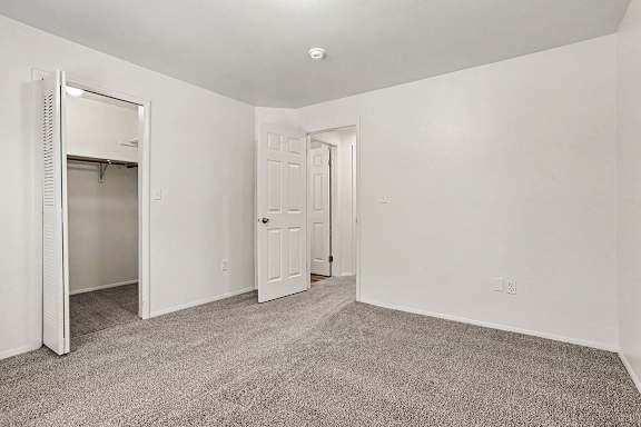 A bedroom with a carpeted floor and a large closet with shelving at Emerald Park Apartments, Kalamazoo, Michigan