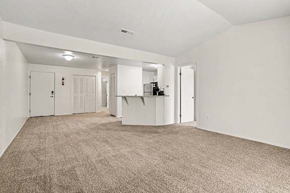 A large, empty living room with a high ceiling and carpeted flooring at Emerald Park Apartments, Kalamazoo, Michigan