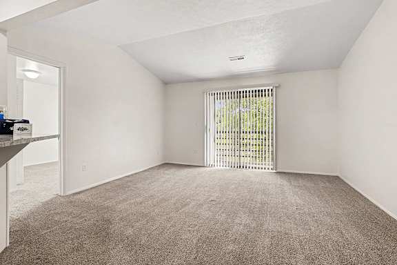 A living room with a carpeted floor and a sliding glass door to a balcony at Emerald Park Apartments, Kalamazoo, Michigan