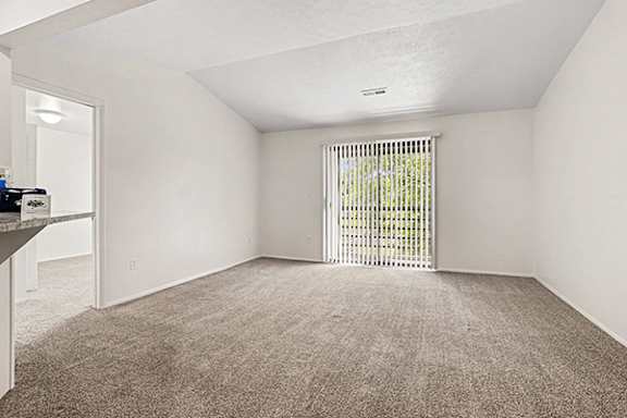 A living room with a vaulted ceiling and a sliding glass door to a balcony at Emerald Park Apartments in Kalamazoo, MI 49001