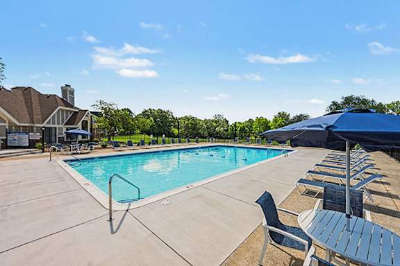 Outdoor swimming pool with lounge chairs and umbrellas at Fairlane Apartments, Springfield, MI