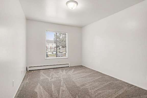 Empty carpeted room with window and baseboard heater at Fairlane Apartments, Springfield, 49037