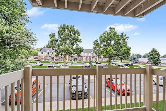 A view from a balcony overlooking a parking lot with cars and a building in the background at Fairlane Apartments in Springfield, MI