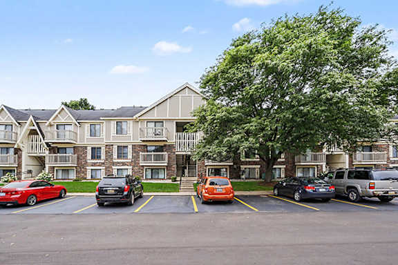 A parking lot with cars and a large apartment building in the background at Fairlane Apartments in Springfield, MI