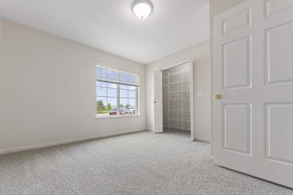 A bedroom with a window, a walk-in closet, and a carpeted floor at Fieldstream Apartment Homes in IA 50023