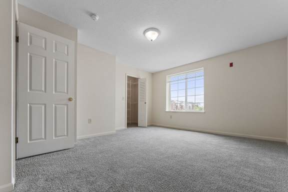 A bedroom with a carpeted floor, large window, and a walk-in closet at Fieldstream Apartment Homes, Iowa