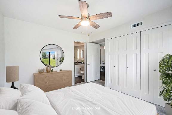 A bedroom with an ensuite, a bed, dresser, mirror, and a ceiling fan at Green Ridge Apartments, Grand Rapids, 49544