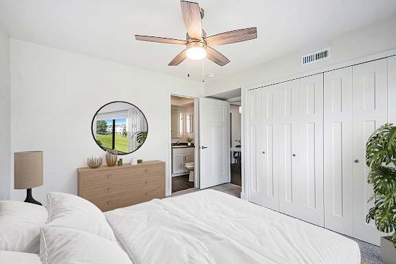 A bedroom with an ensuite, a bed, dresser, mirror, and a ceiling fan at Green Ridge Apartments, Grand Rapids, 49544