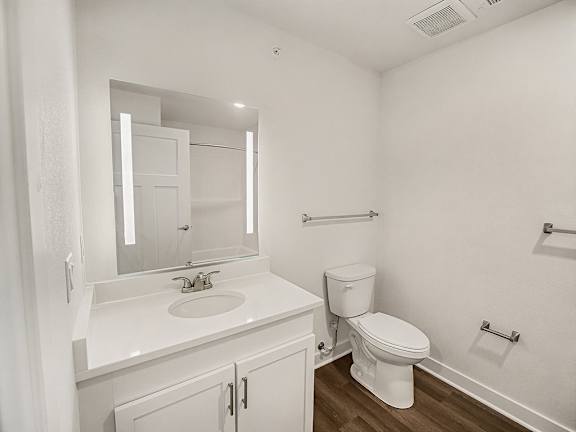A white bathroom with a toilet, sink, and mirror at The Grove Apartment Homes in Lincoln, NE