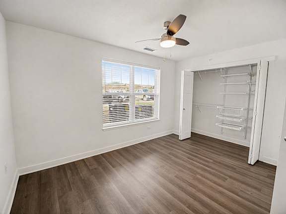 A spacious bedroom with a ceiling fan and a large window with blinds at The Grove Apartment Homes in Lincoln, NE