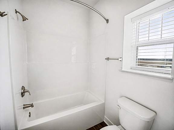 A white bathroom with a toilet and a bathtub at The Grove Apartment Homes in Lincoln, NE