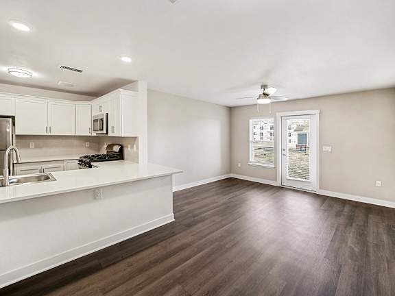 A kitchen with white cabinets and a living room with a ceiling fan at The Grove Apartment Homes in Lincoln, NE