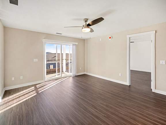 A living room with a ceiling fan and sliding glass doors to a balcony at The Grove Apartment Homes in Lincoln, NE
