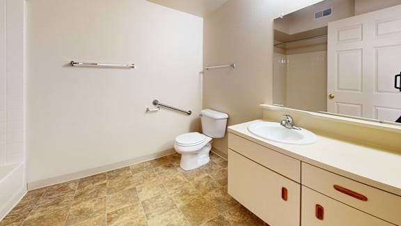 A bathroom with a toilet, sink, and mirror at Gull Prairie/Gull Run Apartments and Townhomes in Kalamazoo, MI