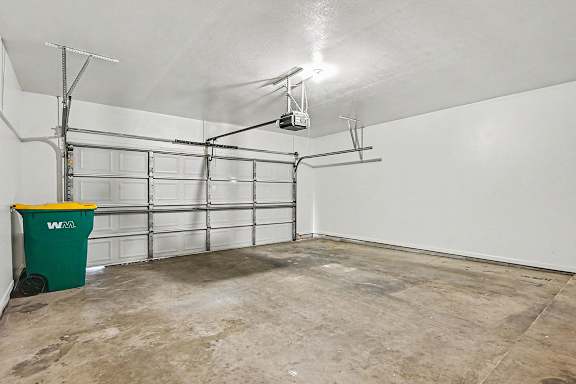 A garage with a green trash can and a white wall.