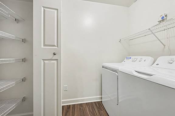 A white ironing board in a small room with a door and a shelf.