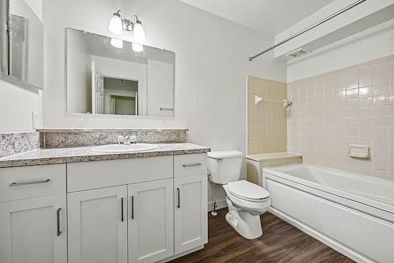 A white bathroom with a marble countertop and wooden flooring.