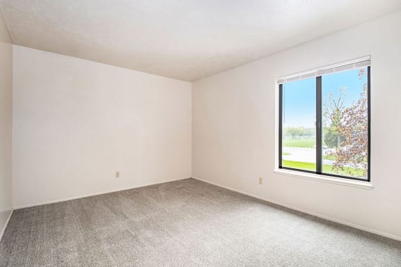 an empty bedroom with a large window and carpeting at Hickory Village Apartments, Indiana, 46545