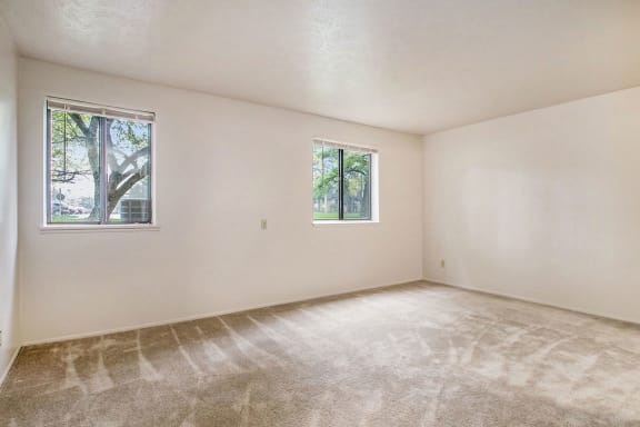 an empty living room with carpet and two windows at Hickory Village Apartments, Mishawaka, Indiana