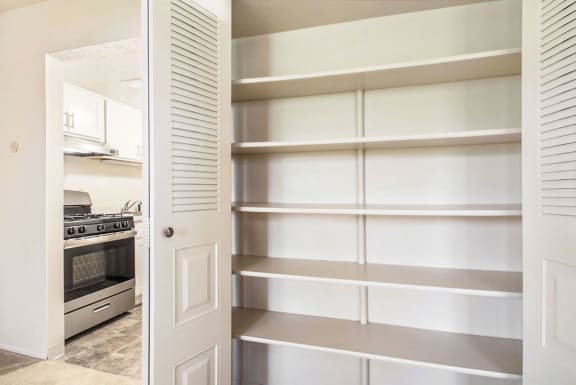 a pantry with white shelving and a kitchen with a stove and at Hickory Village Apartments, Indiana