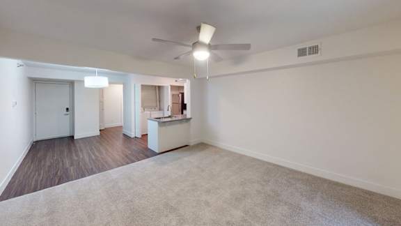 A spacious living and dining room with a carpeted floor and a ceiling fan