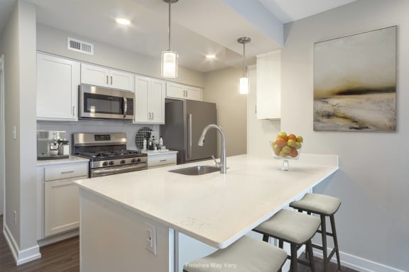 a kitchen with white cabinets and a white island with two stools at Hillside Apartments, Wixom, MI