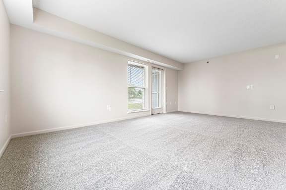 A spacious living room with a carpeted floor and a french door to a patio at Hunters Pond Apartment Homes, Champaign, IL