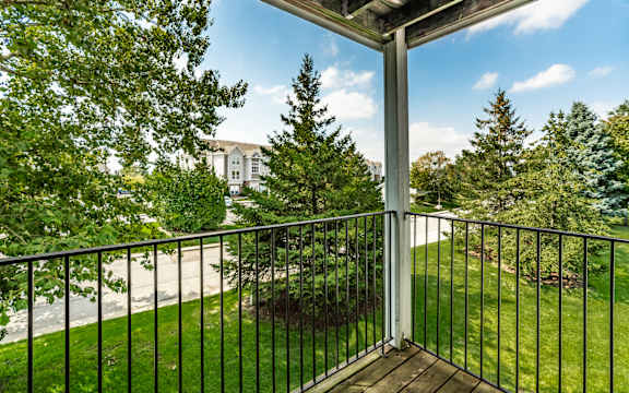 A balcony with a black railing and a view of a tree and a building at Huntington Cove Apartments, Merrillville, IN