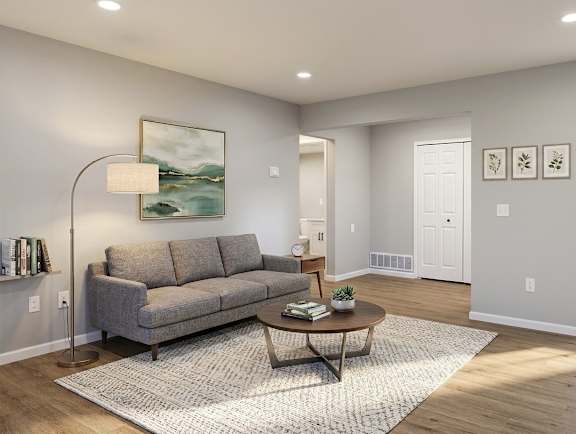 A living room with a grey couch, a round table, and a painting on the wall.