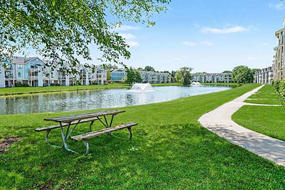 A picnic table sits on a grassy area next to a pond at Indian Lakes Apartments in Mishawaka, IN