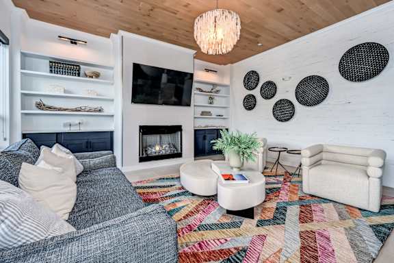 A living room with a grey couch, a white armchair, a white coffee table, a fireplace, and a wooden ceiling at Ironwood Flats Apartments, Brandon