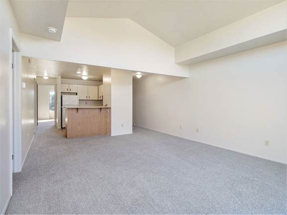 A spacious living and dining room with a cathedral ceiling and a kitchen in the background at Liberty Mills Apartments, Fort Wayne