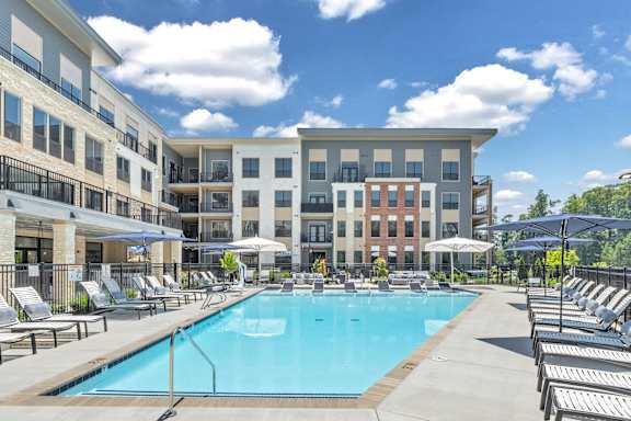 A large swimming pool surrounded by sun loungers and umbrellas in front of a multi-story apartment building at Luxe 360 on Centerpointe Apartments, Midlothian